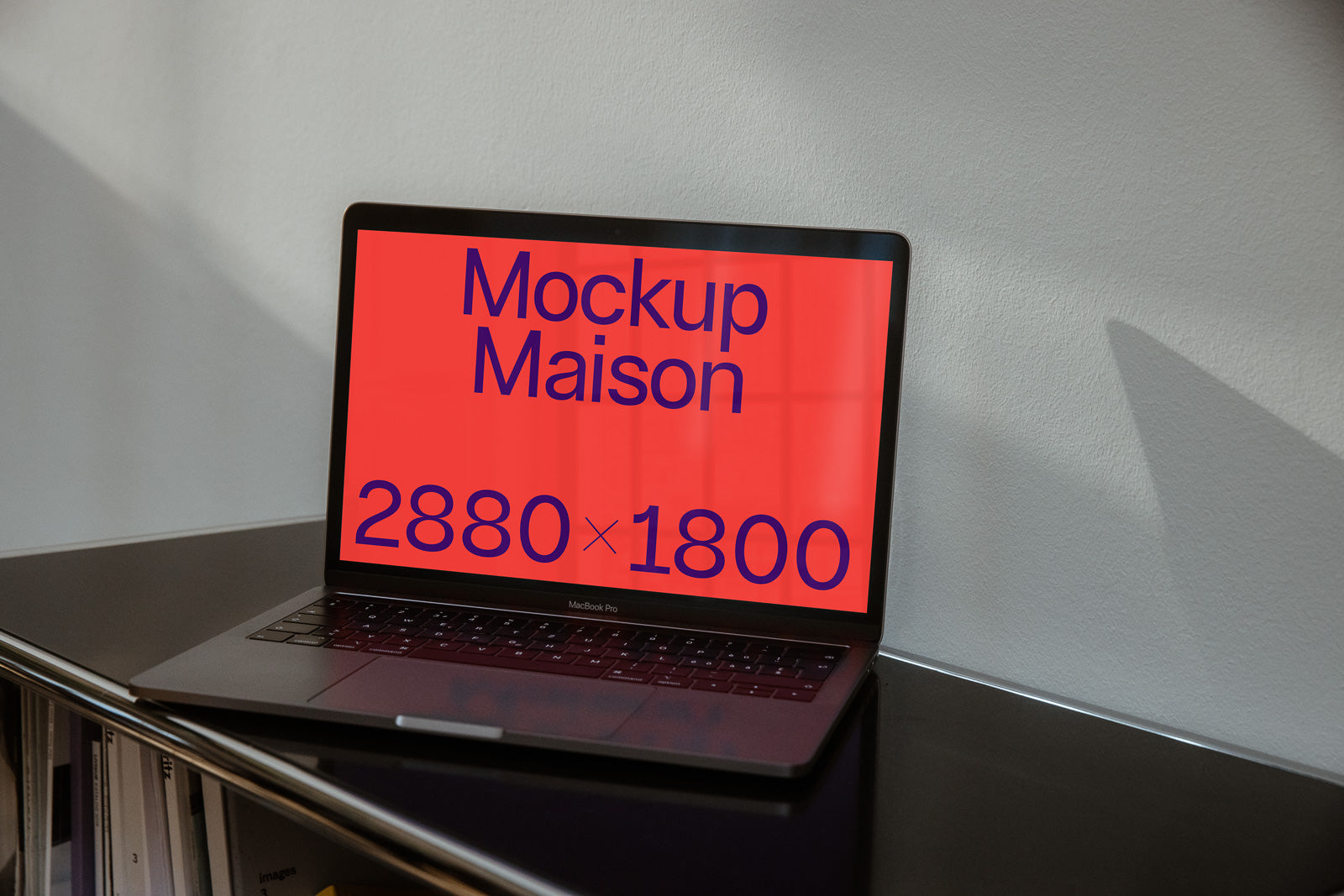 PSD mockup of a laptop on a desk against a wall, displaying the text "Mockup Maison 2880 × 1800" on a bright red screen.