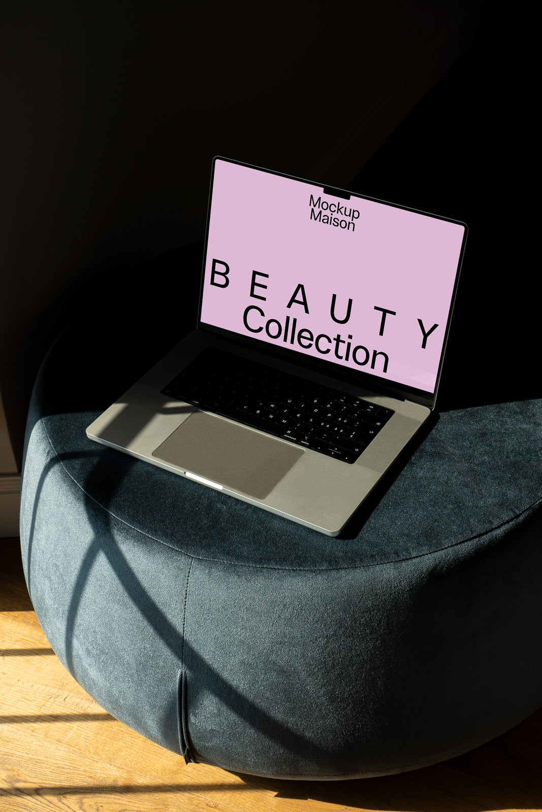 PSD mockup of a laptop displaying "Beauty Collection" on a pink screen, placed on a blue ottoman with sunlight streaming in, creating soft shadows.