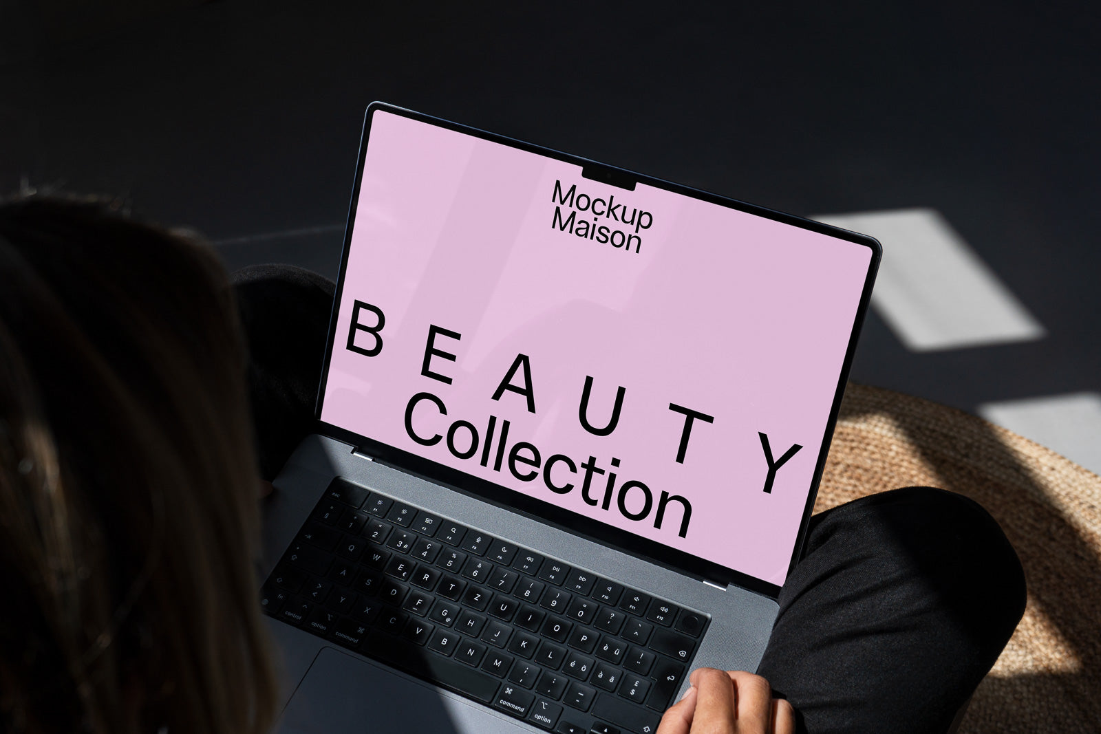 PSD mockup of an open laptop displaying a pink screen with "Mockup Maison" and "Beauty Collection" in bold text, held by a person.