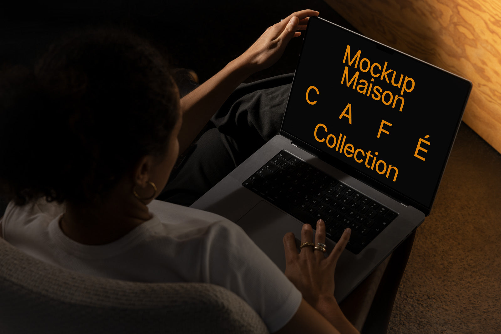 PSD mockup of a person using a laptop displaying the text "Mockup Maison CAFE Collection" in bold orange letters on a dark screen.