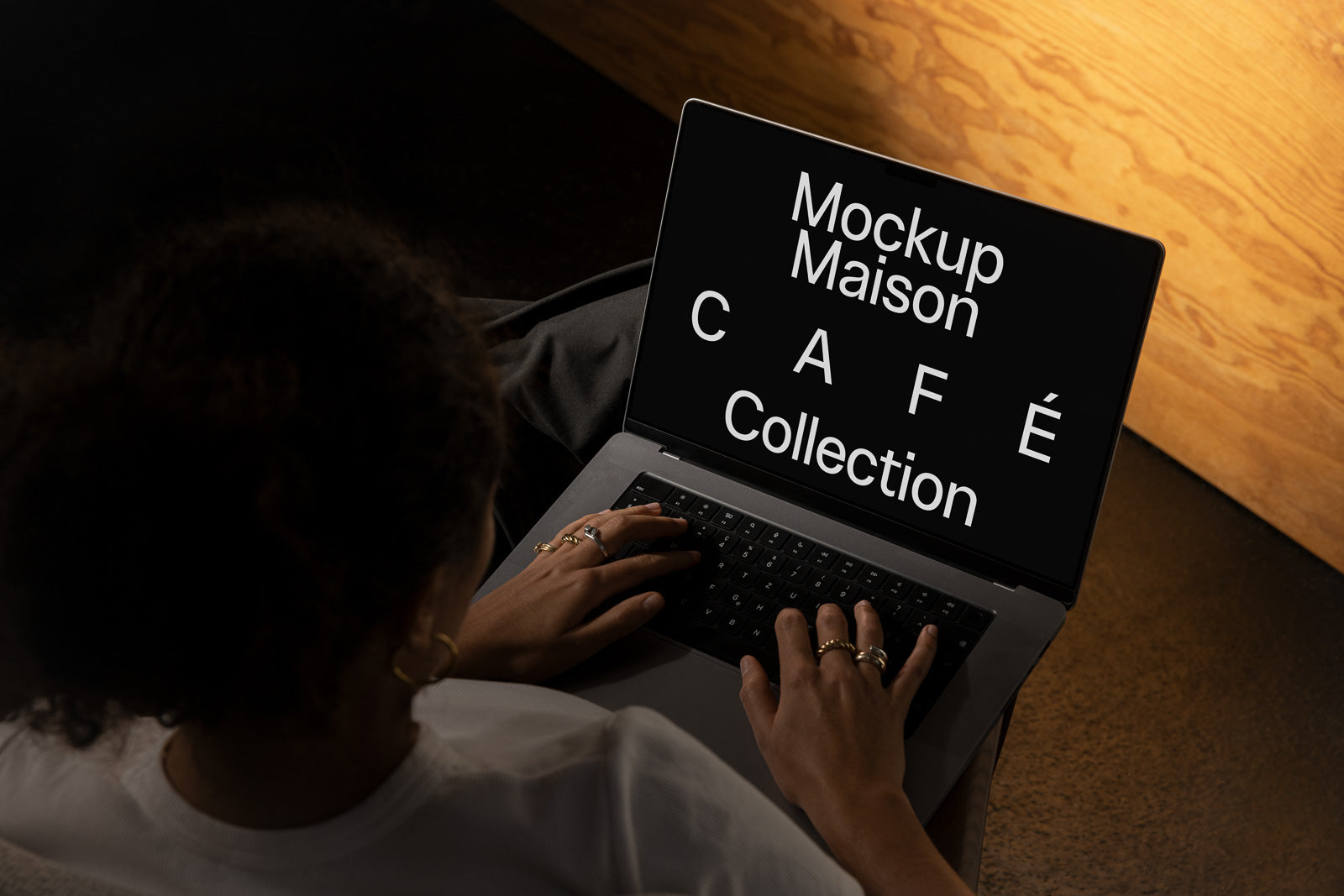 PSD mockup of a laptop screen displaying "Mockup Maison Café Collection" in white text viewed by a person with curly hair, wearing rings and earrings.