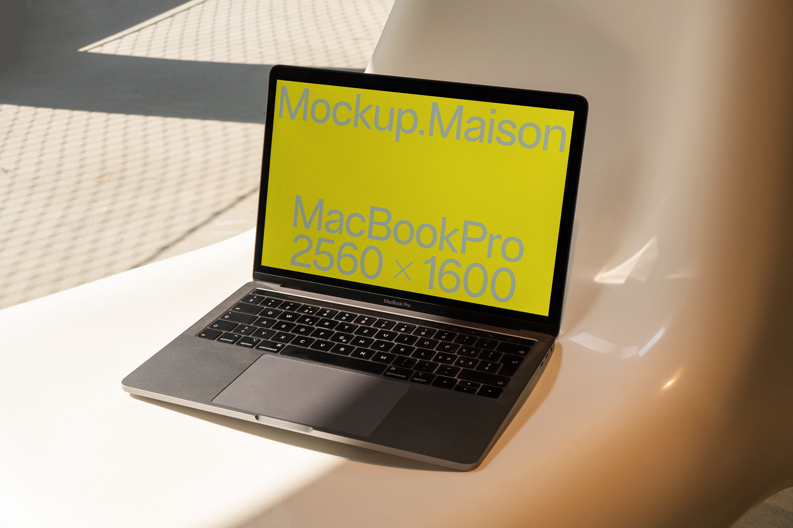 PSD mockup of a MacBook Pro with a yellow screen displaying "Mockup.Maison" and screen resolution "2560 × 1600" in a brightly lit setting.