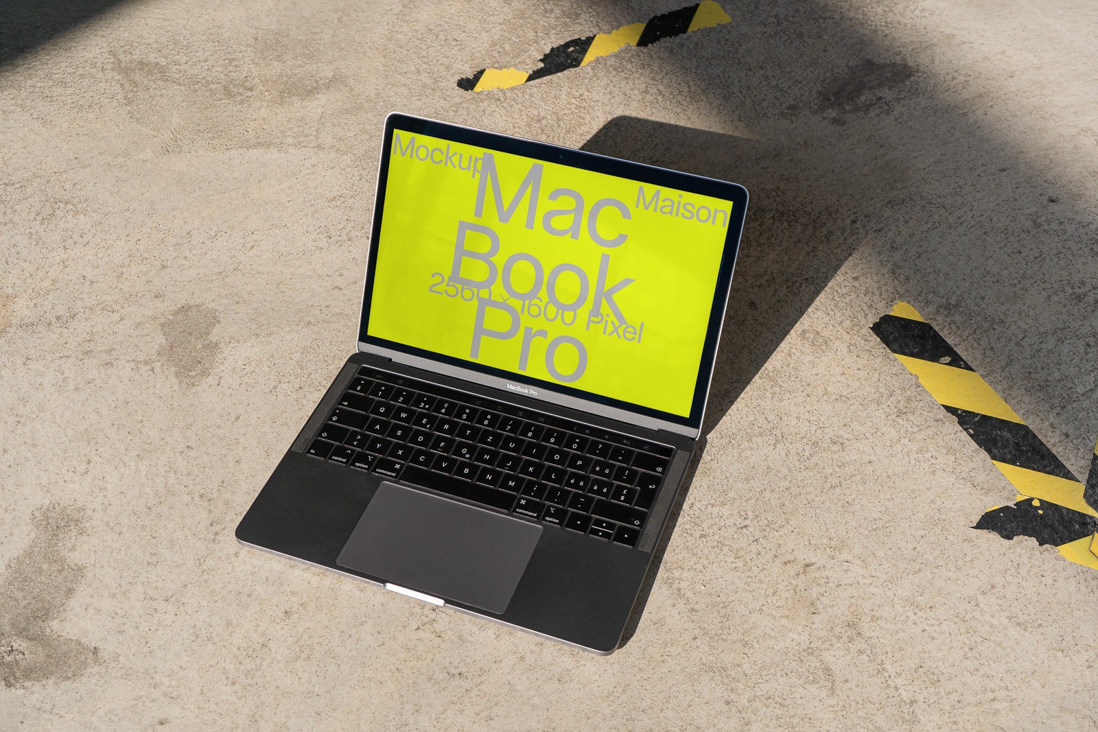 PSD mockup of a MacBook Pro on a concrete surface with a yellow screen displaying text. Diagonal black and yellow tape is visible on the ground.
