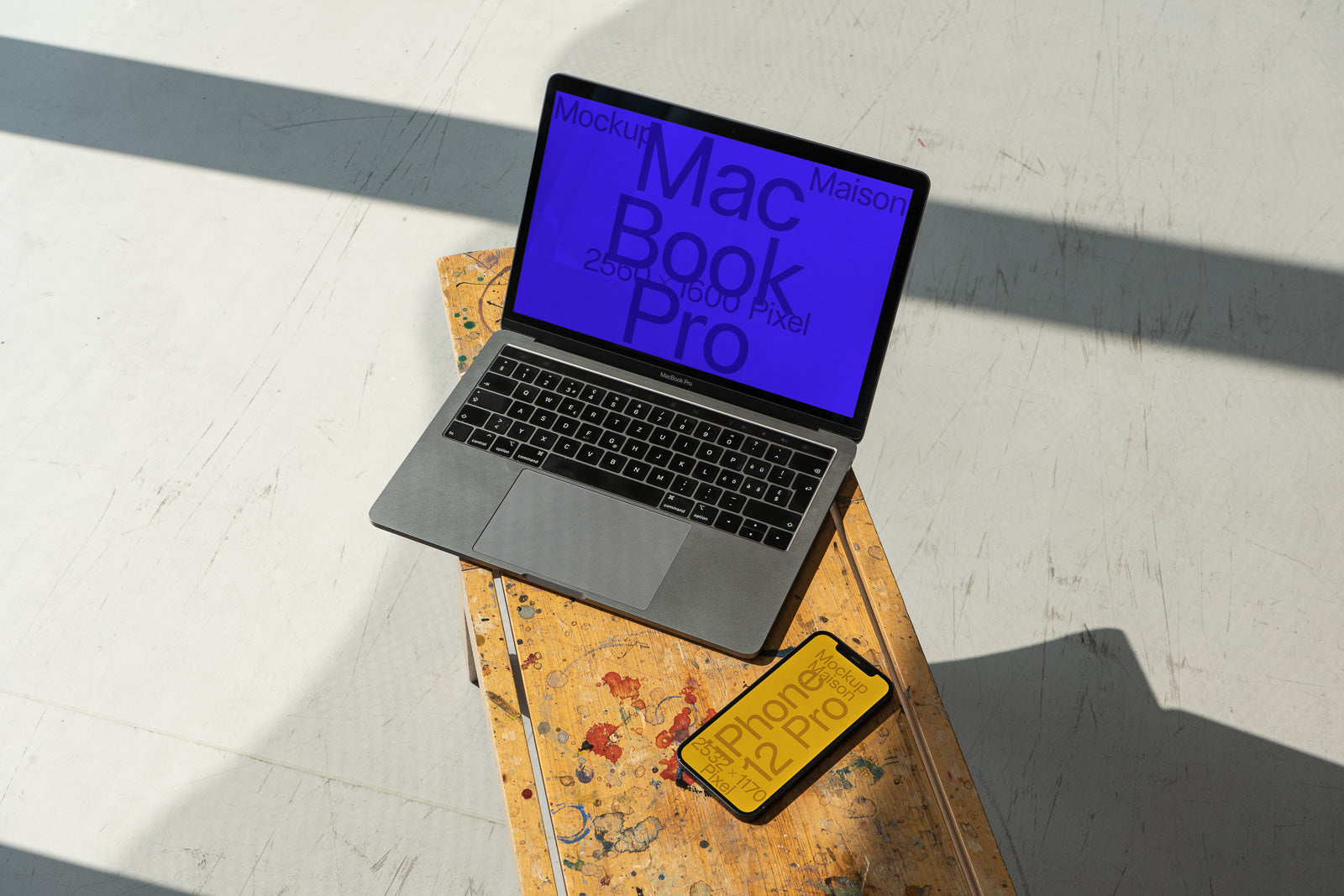 PSD mockup of a MacBook Pro with blue screen displaying bold text, placed on a rustic wooden surface, alongside an iPhone with a yellow screen.