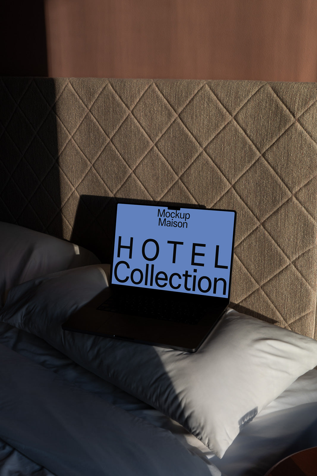 PSD mockup of a laptop on a bed with a textured headboard, displaying text that reads "Hotel Collection" on the screen.