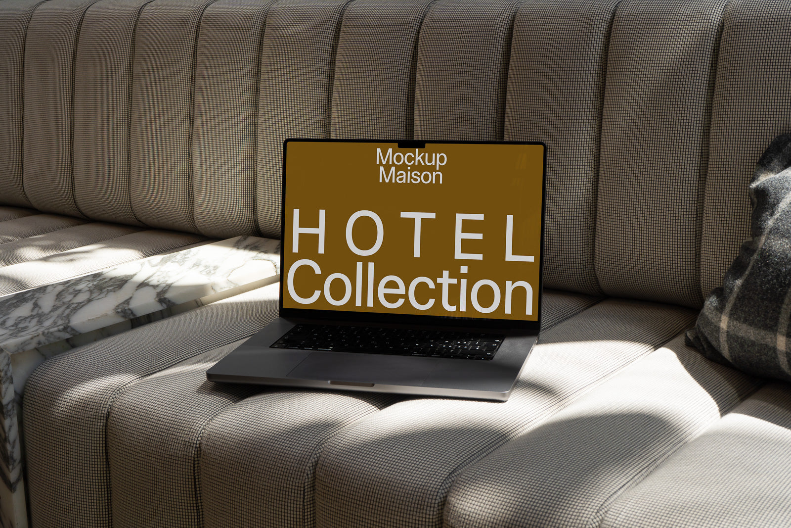 PSD mockup of a modern laptop on a patterned sofa, displaying "Mockup Maison Hotel Collection" on the screen against a brown background.