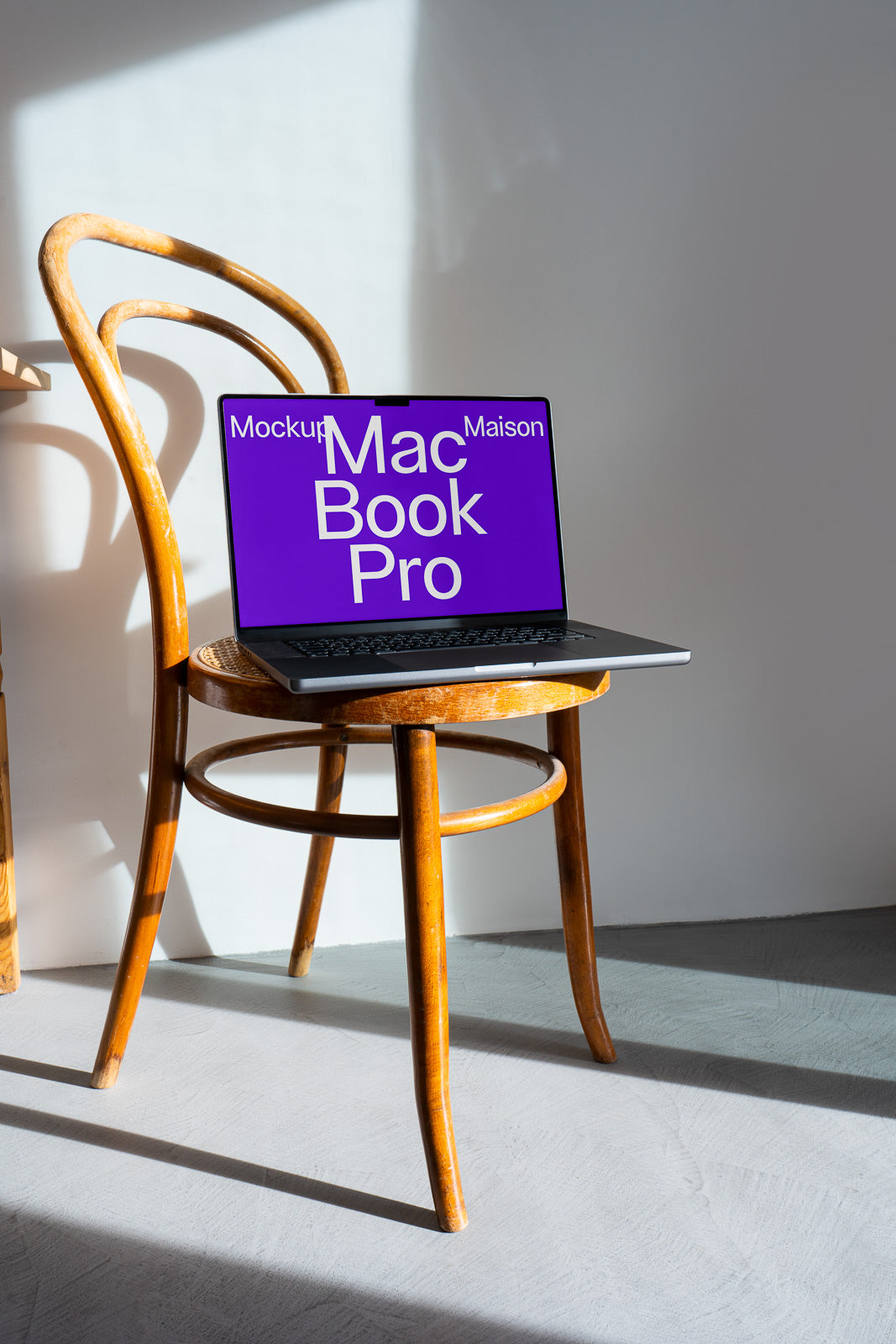 PSD mockup of a MacBook Pro on a wooden chair with sunlight casting shadows on the floor and wall in a minimalist setting.
