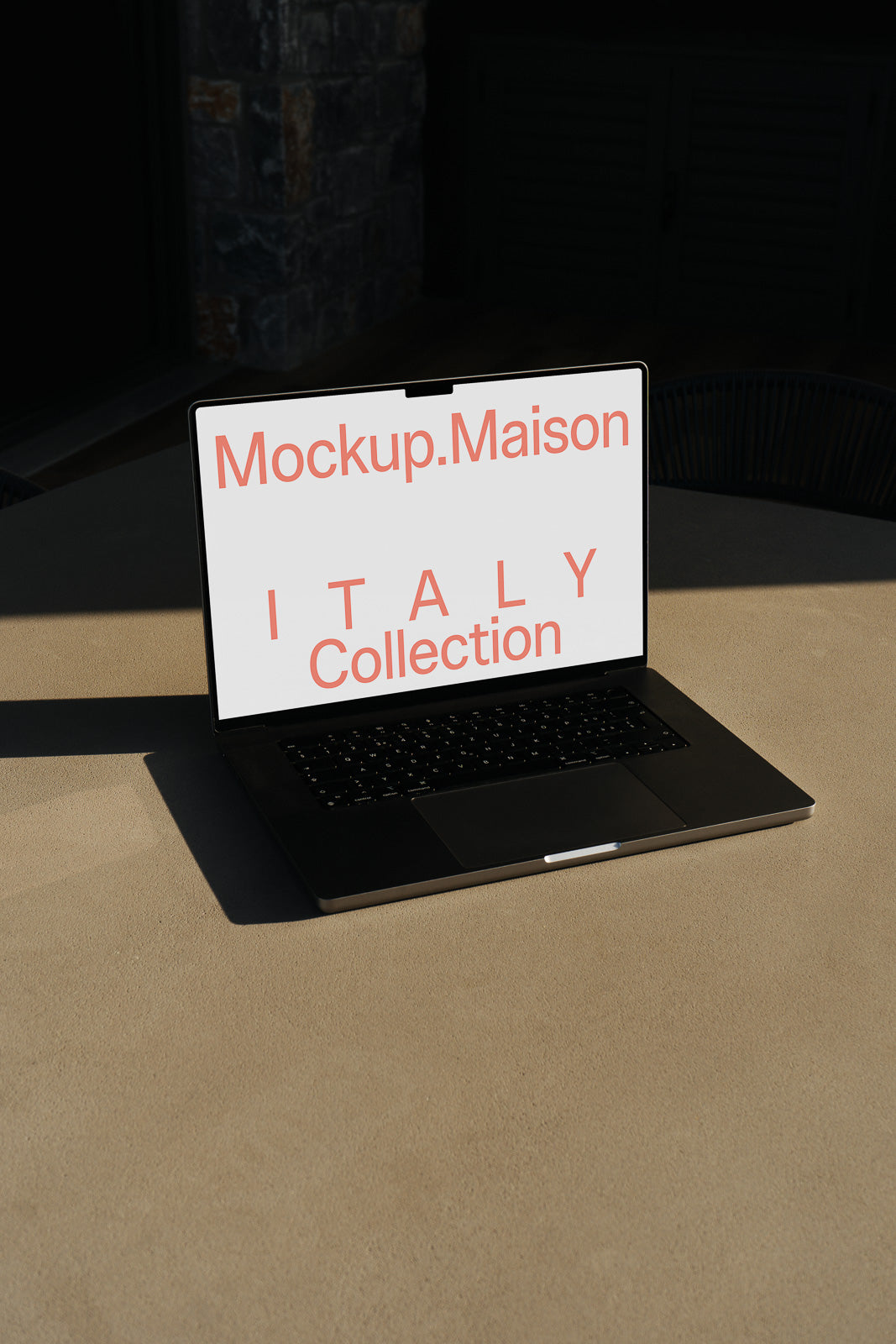 PSD mockup of a laptop on a sunlit table displaying "Mockup.Maison ITALY Collection" on the screen.