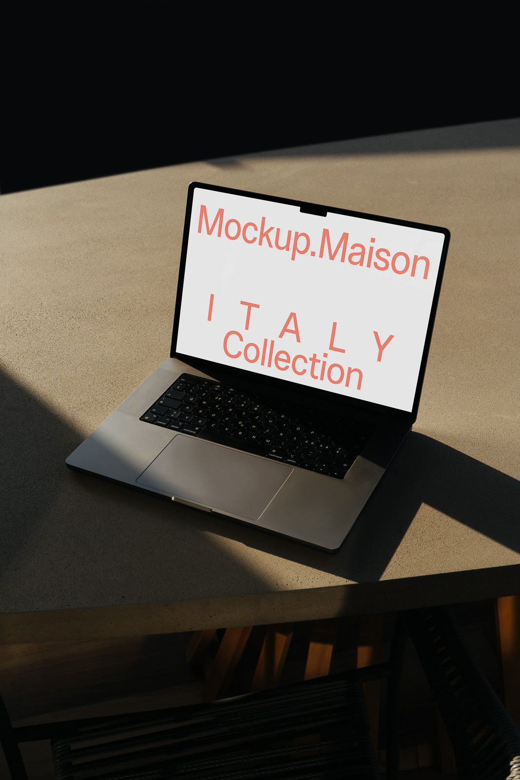 PSD mockup of a laptop on a table displaying the text "Mockup.Maison ITALY Collection" on its screen. Natural sunlight creates a shadow effect.