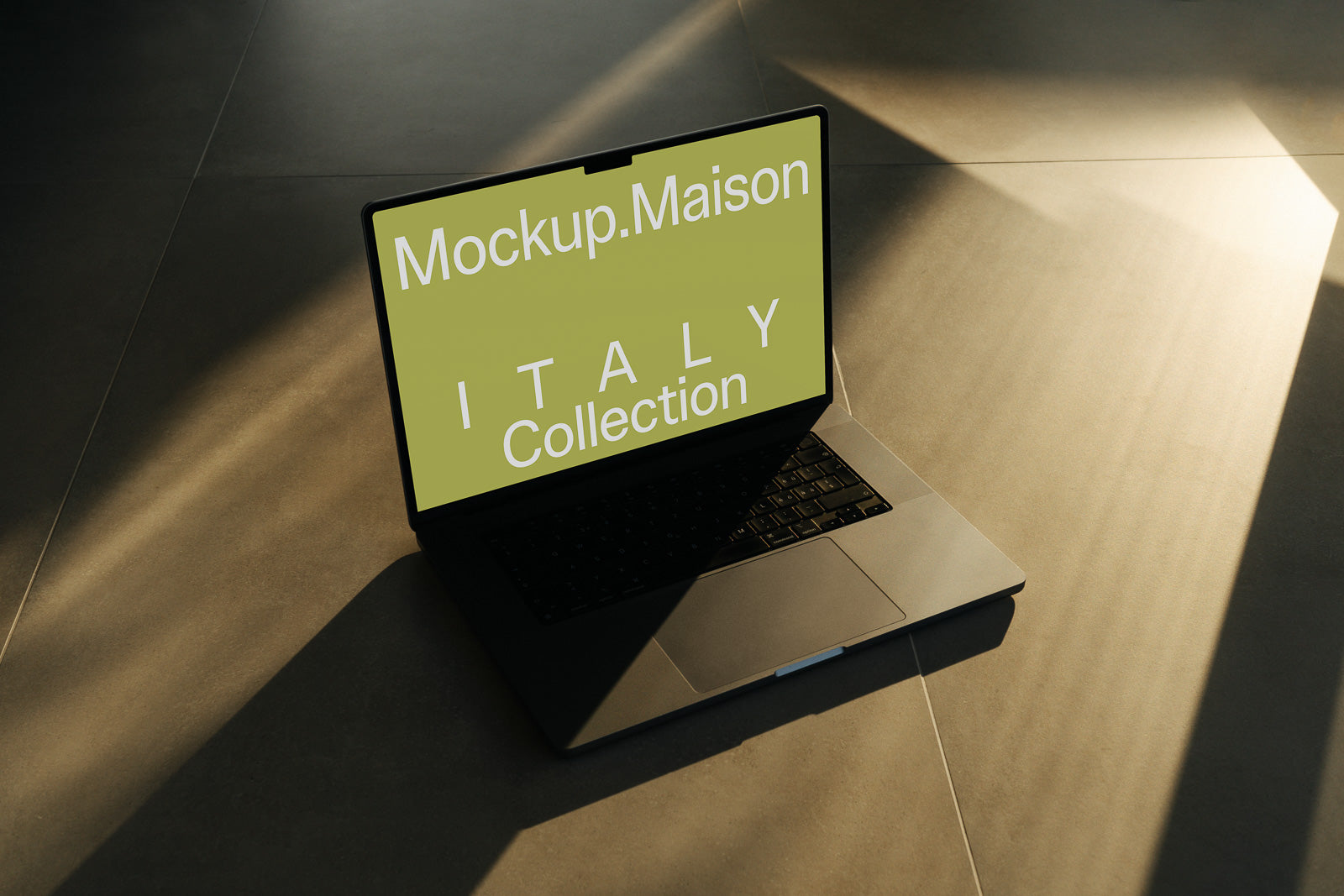 PSD mockup of a laptop on a tiled floor, screen displaying "Mockup.Maison ITALY Collection" in white text on a green background.