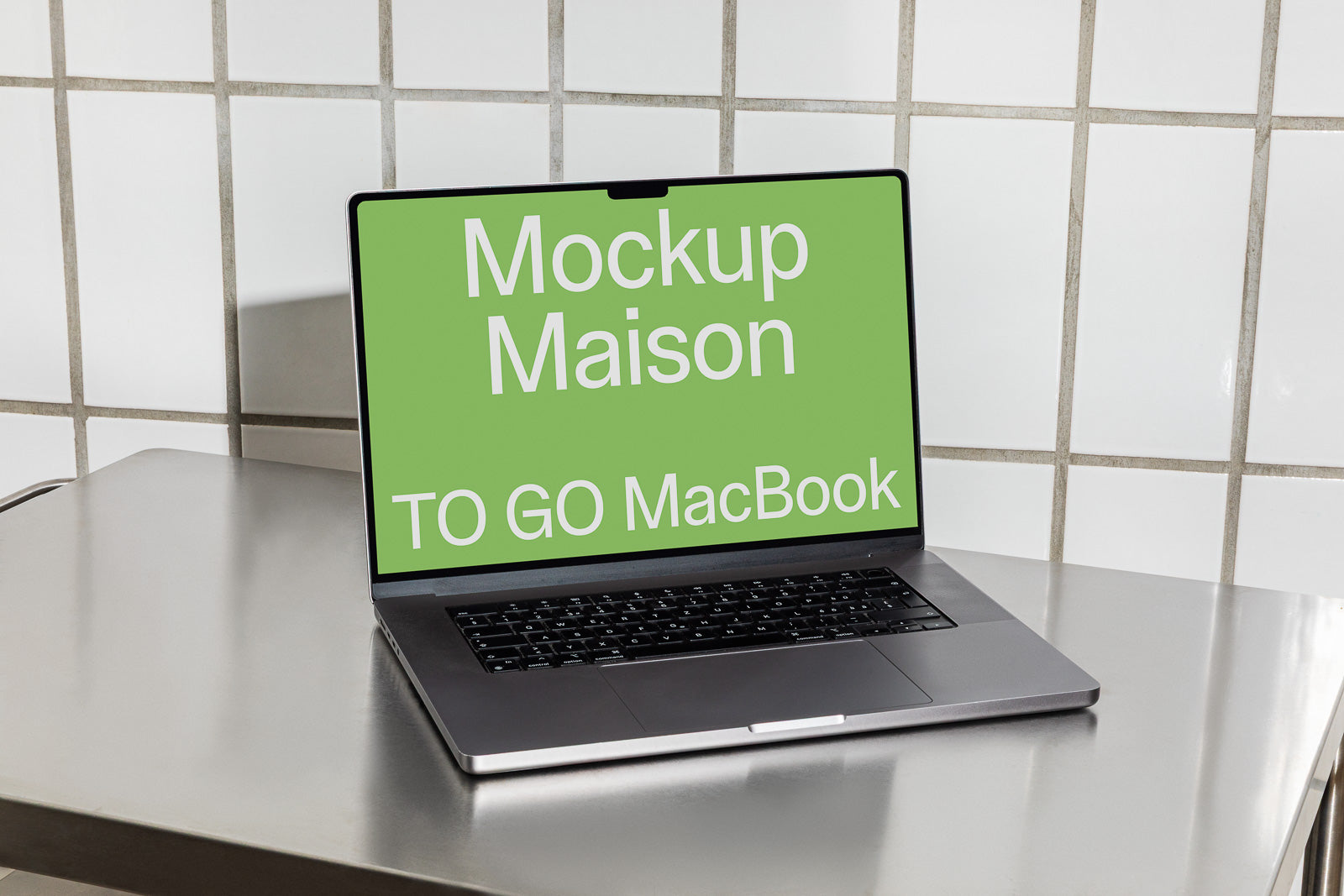 PSD mockup of a MacBook open on a metal table against a tiled wall, displaying a green screen with the text "Mockup Maison TO GO MacBook" in white.
