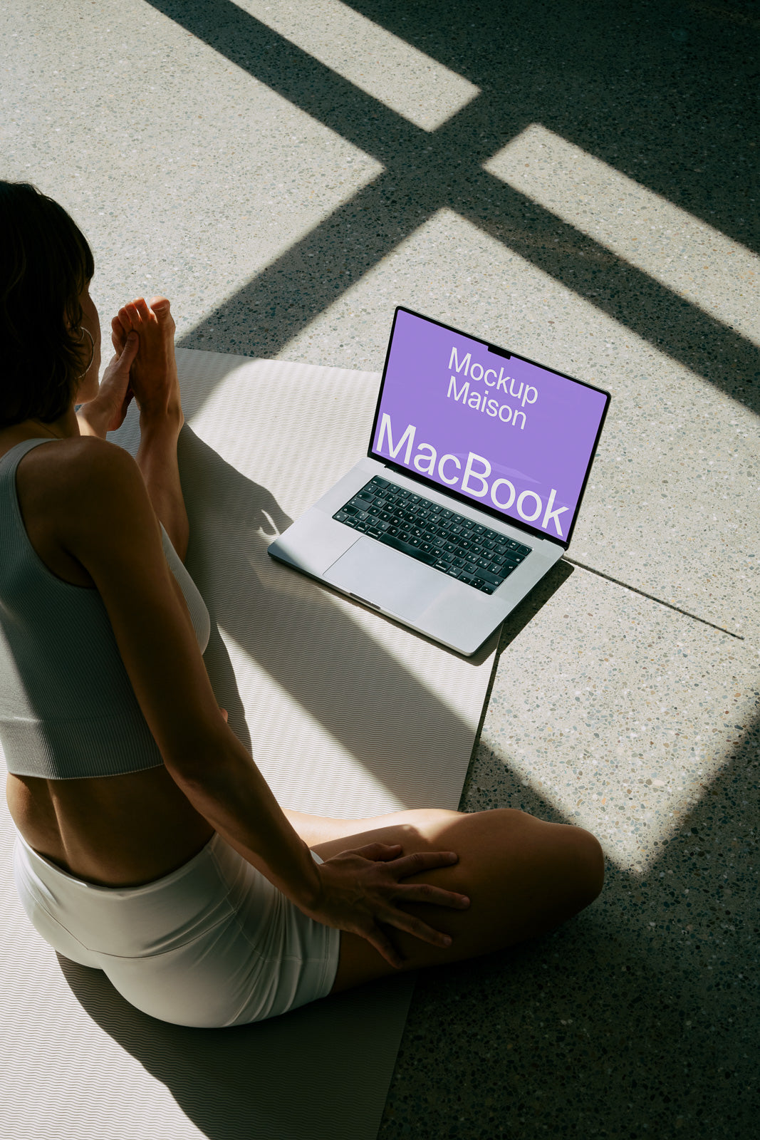 PSD mockup of a MacBook on the floor with a person sitting beside it, sunlight creating patterns on the floor.