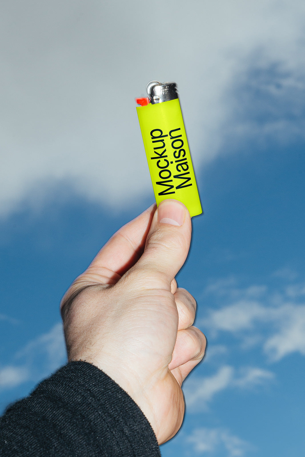 PSD mockup of a hand holding a bright green lighter labeled "Mockup Maison" against a blue sky.
