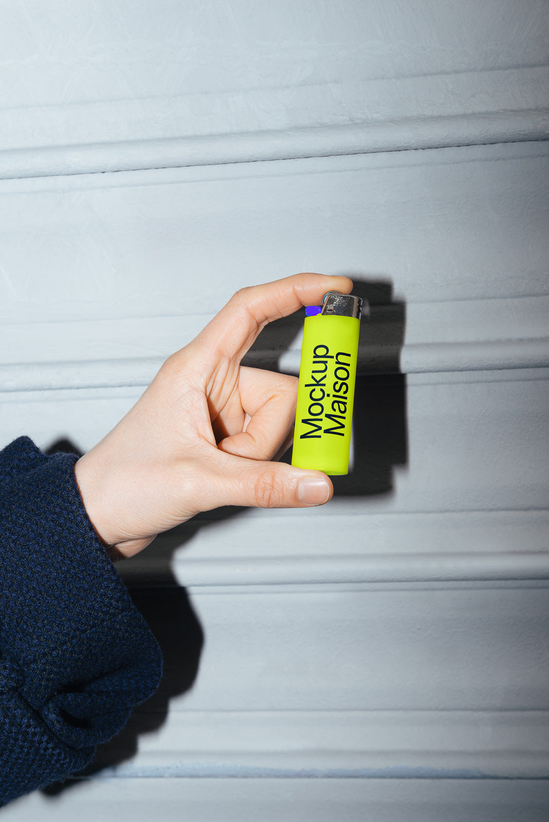 PSD mockup of a hand holding a green lighter with the text "Mockup Maison" displayed prominently, against a textured gray background.