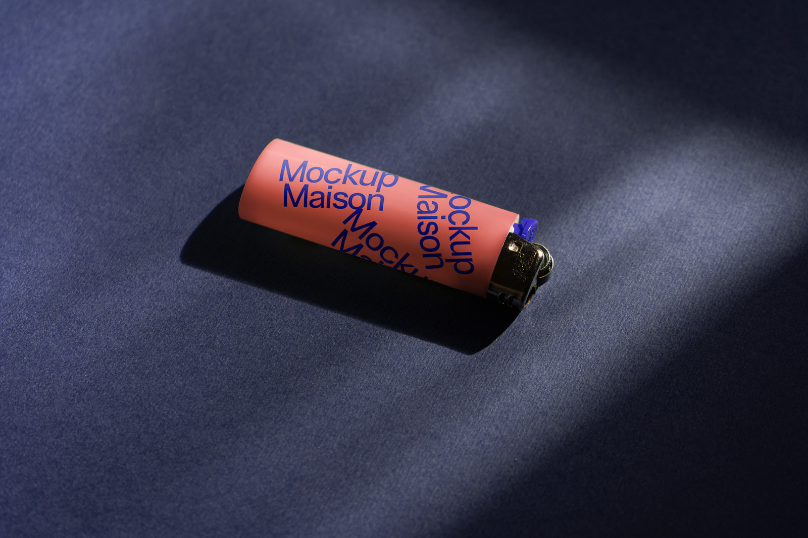 PSD mockup of a pink lighter with blue "Mockup Maison" text, lying on a dark textured surface with soft lighting and shadows.