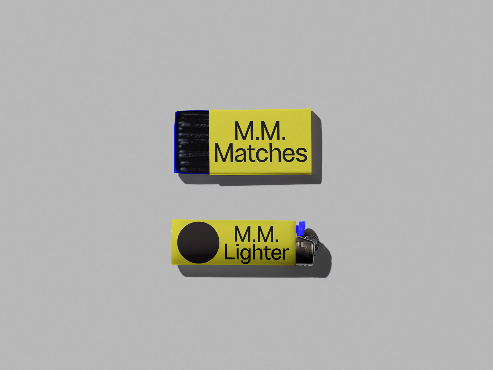 PSD mockup of yellow matchbox and lighter, both labeled "M.M." against a gray background, highlighting a minimalist design.
