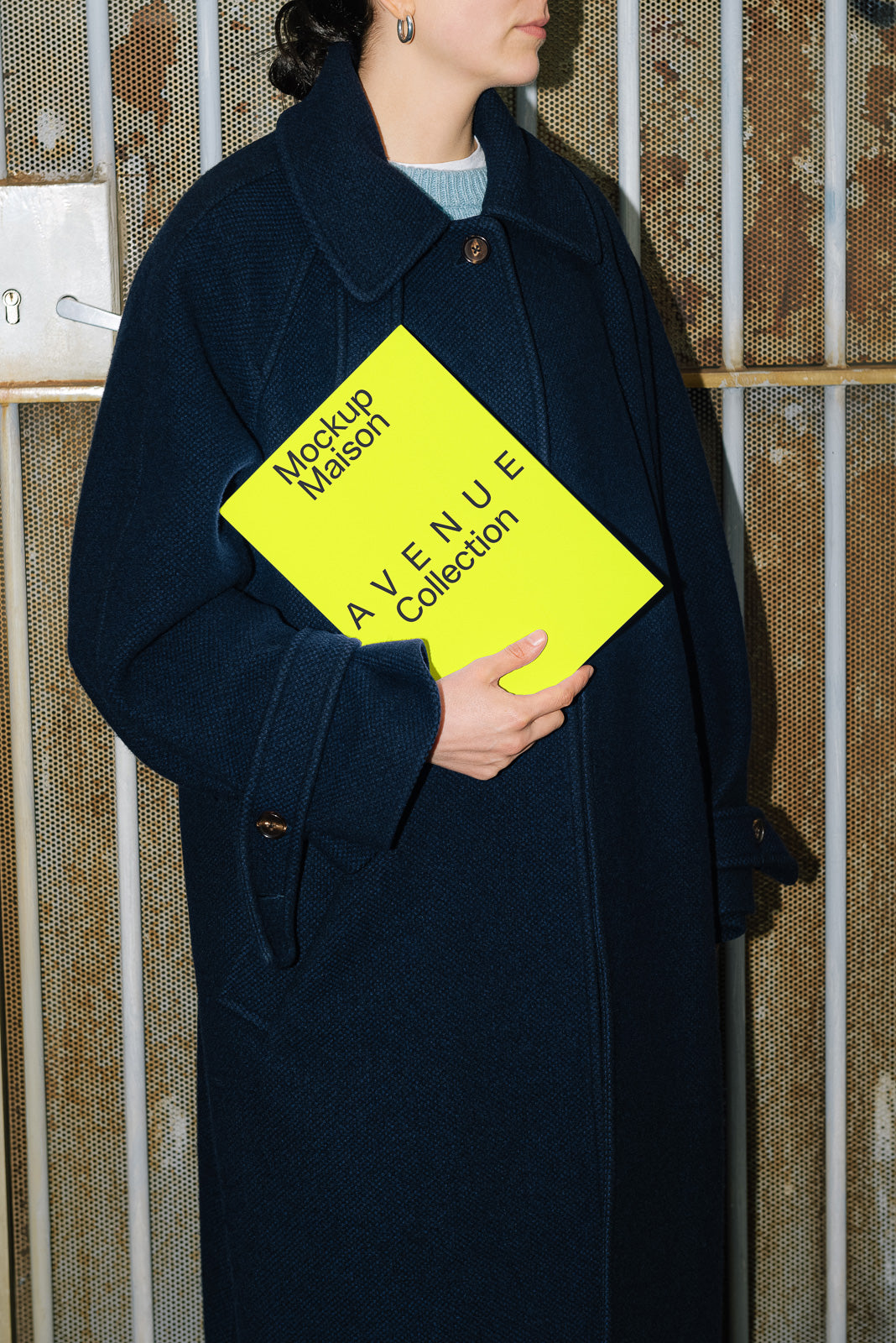 PSD mockup of a person holding a bright yellow booklet titled "Avenue Collection" with "Mockup Maison" branding, against a textured background.