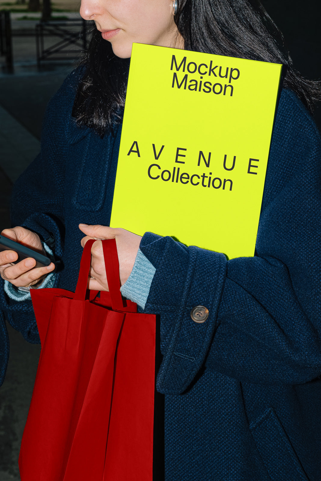 PSD mockup of a person holding a bright yellow book titled "Avenue Collection" and a red paper bag while using a smartphone.