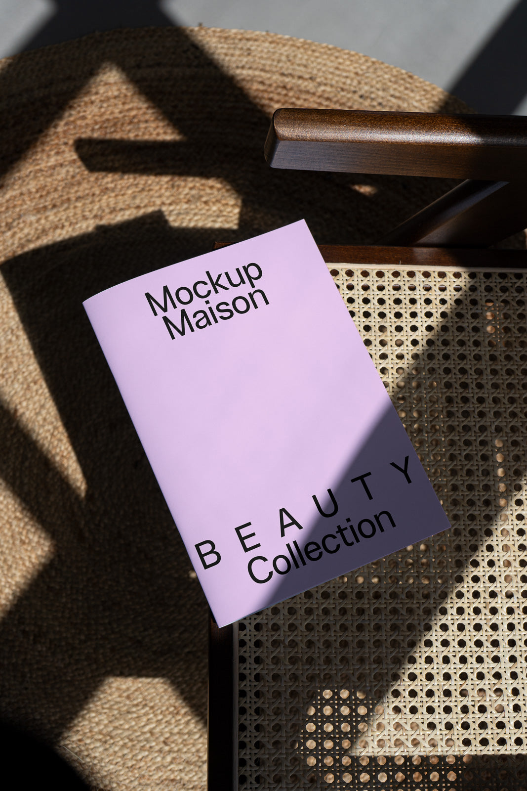 PSD mockup of a lavender booklet titled "Mockup Maison BEAUTY Collection" resting on a woven chair, with shadows cast on both surfaces.
