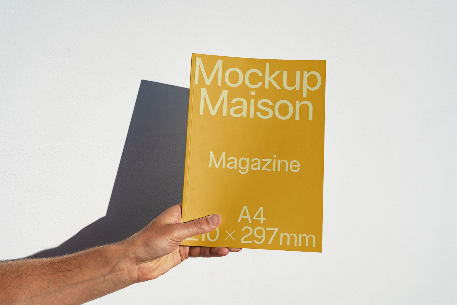 PSD mockup of a hand holding a yellow magazine cover against a white background, featuring the text "Mockup Maison Magazine A4 210 x 297 mm."
