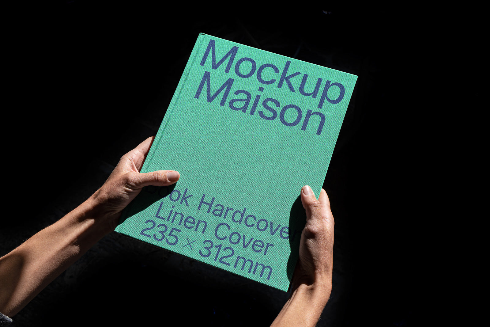 PSD mockup of a green hardcover book with linen texture, titled "Mockup Maison," indicating dimensions 235 x 312mm, held by hands against a dark background.