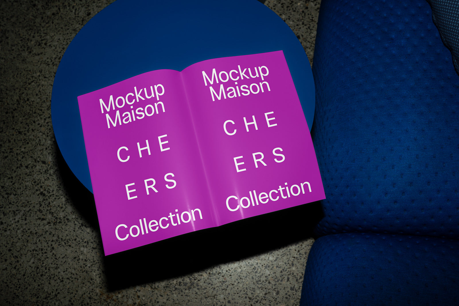 PSD mockup of an open magazine on a blue table, featuring "Mockup Maison" and "CHEERS Collection" in white on a vibrant purple background.