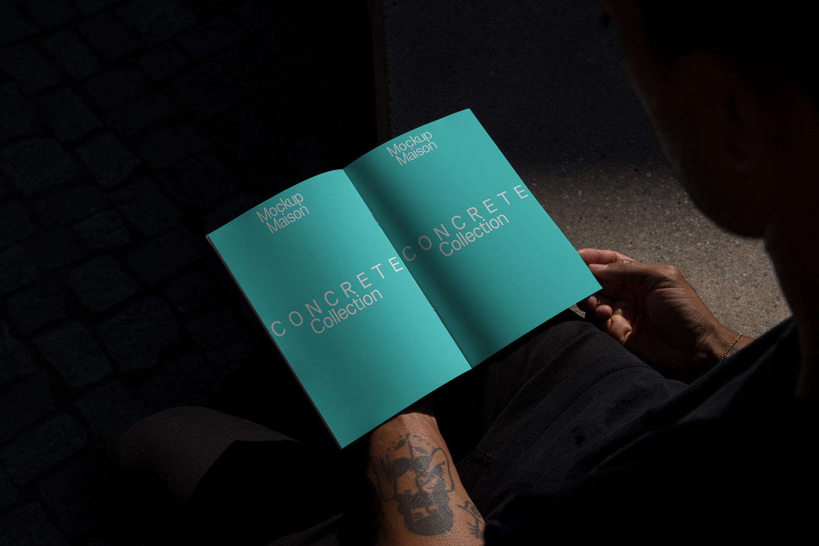 PSD mockup of a person holding an open brochure titled "Concrete Collection" with a matte turquoise cover, sitting in a shadowed area.