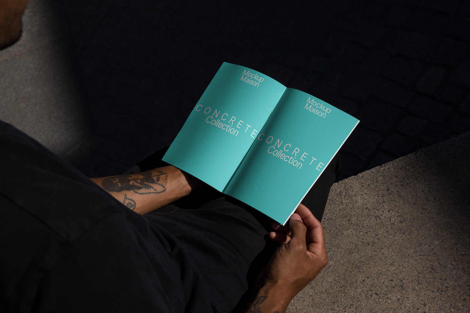 PSD mockup of an open booklet titled "Concrete Collection" held by tattooed hands, set outdoors with shadows casting over the pages.