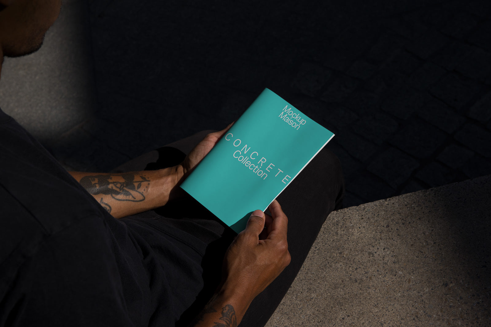 PSD mockup of a person holding a teal booklet labeled "CONCRETE Collection" and "MockUp Maison" while seated on steps.