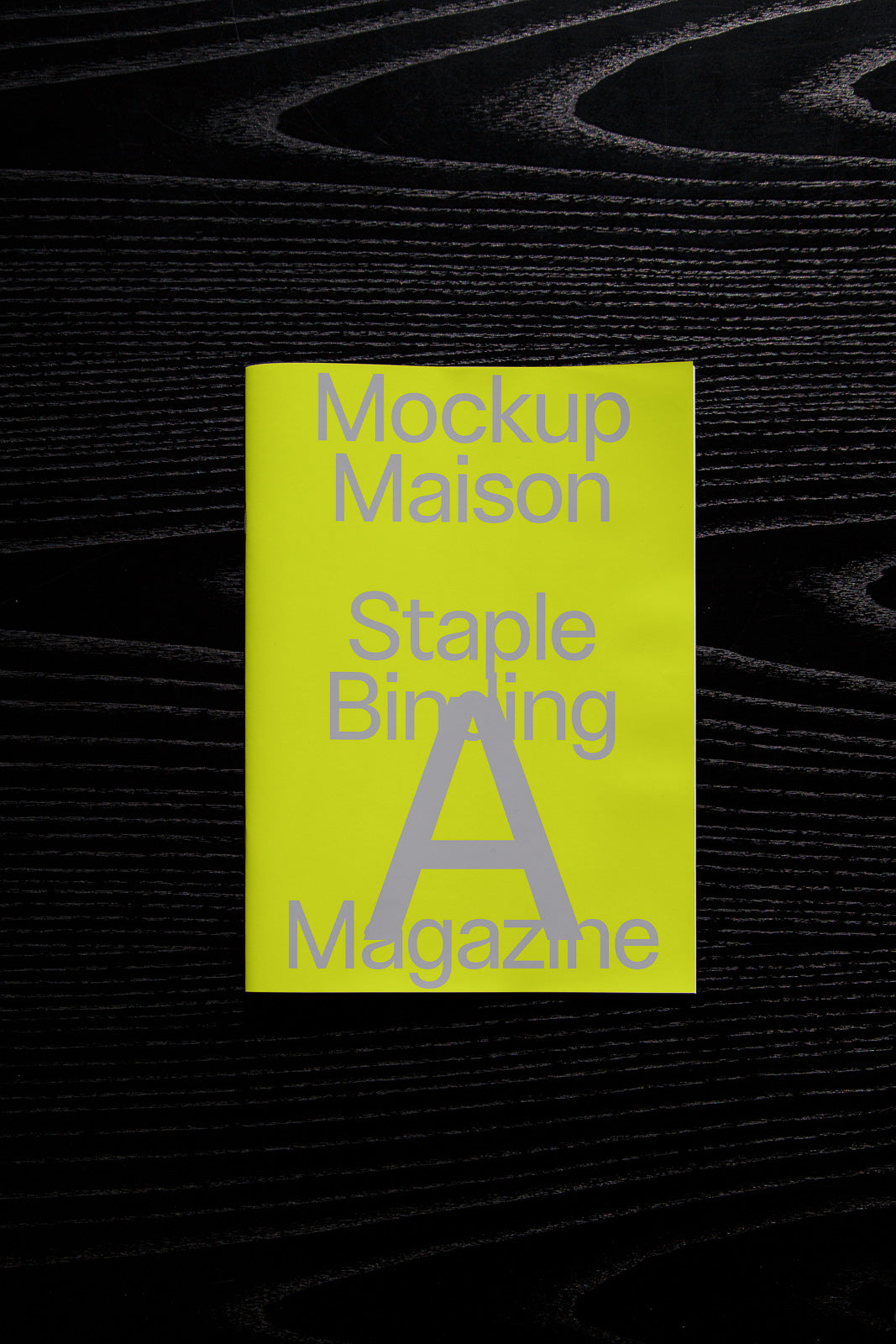 PSD mockup of a staple-bound magazine with a bright yellow cover featuring large, bold gray text against a dark wooden surface.