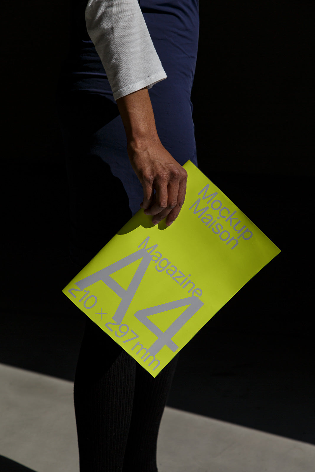 PSD mockup of a person holding a vibrant yellow A4 magazine with gray text in a dimly lit setting, highlighting the magazine’s modern design.