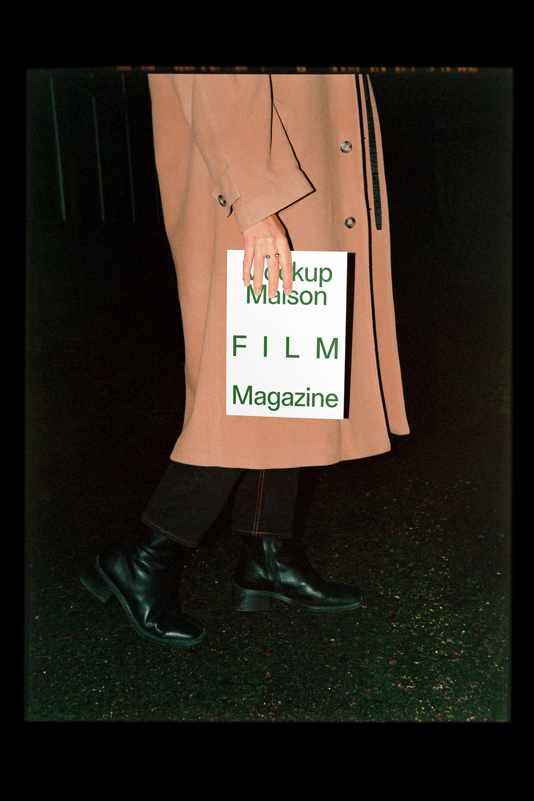 PSD mockup of a person holding a magazine with the text "Mockup Maison FILM Magazine" in green letters, wearing a beige coat and black boots.