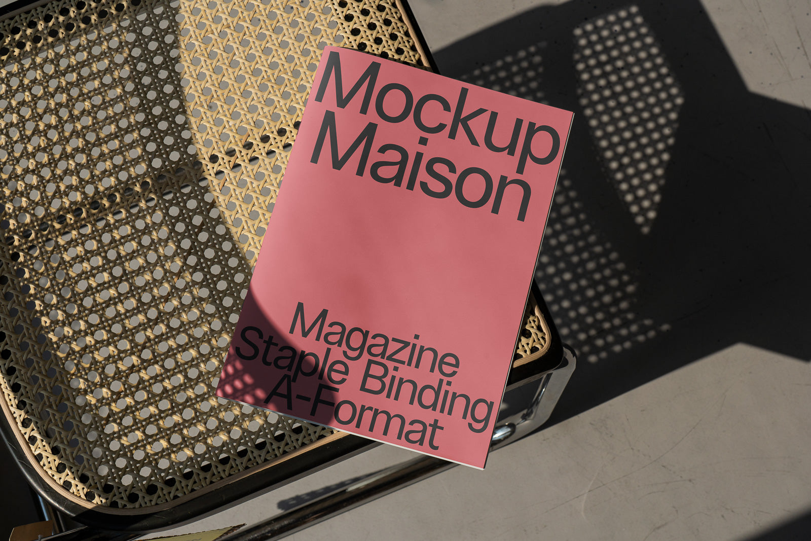 PSD mockup of a pink magazine cover with bold black text titled "Mockup Maison" on a woven chair, casting shadows on the ground.
