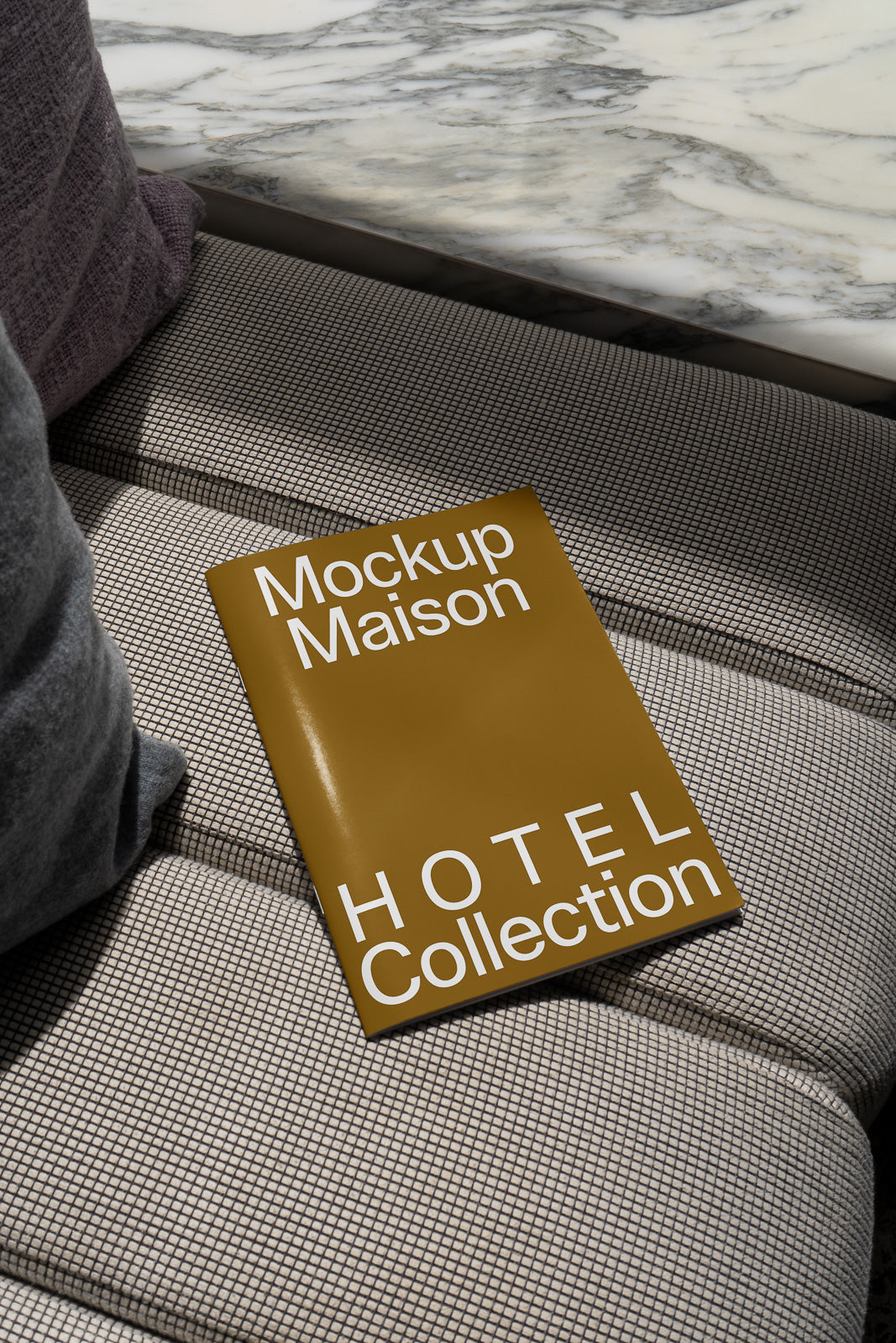 PSD mockup of a magazine titled "Mockup Maison Hotel Collection" on a textured sofa near a marble table background.