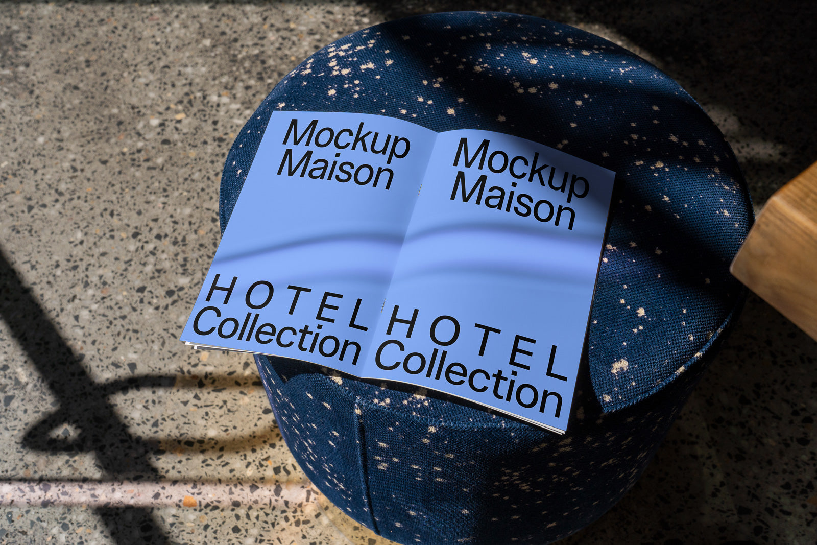 PSD mockup of an open booklet titled "Mockup Maison" on a blue, speckled ottoman, with "Hotel Collection" text, casting shadows on a terrazzo floor.