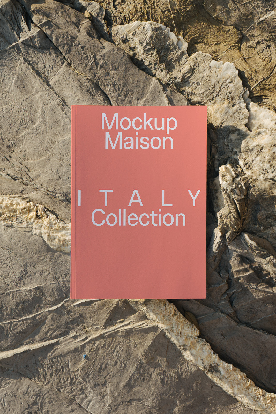 PSD mockup of a pink book with "Mockup Maison" and "ITALY Collection" text, placed on textured stone surface.