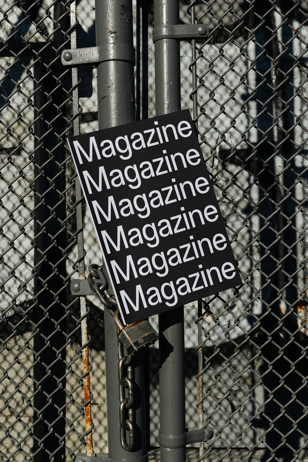PSD mockup of a magazine cover with repeated "Magazine" text, leaning against a metal gate with a chain and padlock.