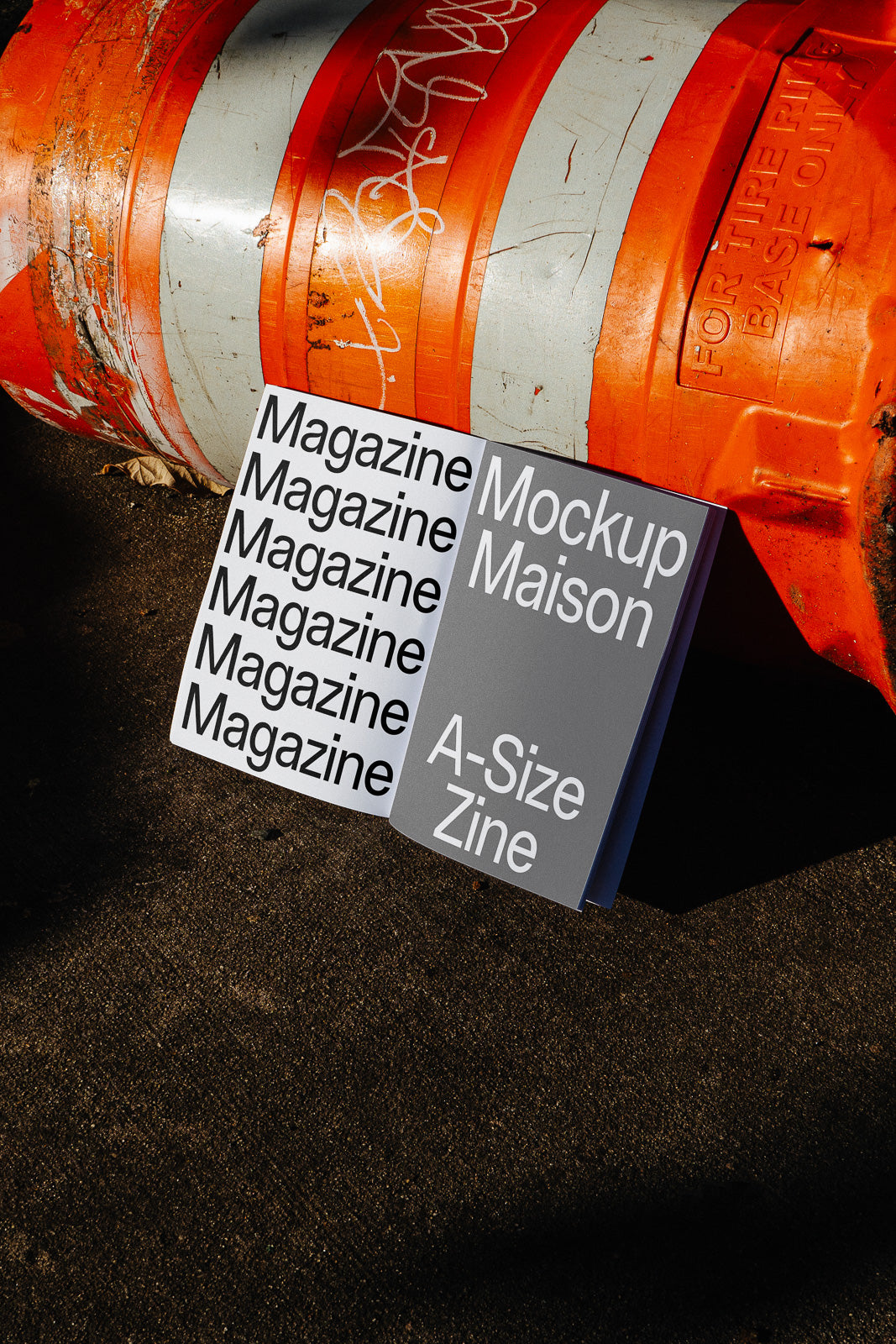 PSD mockup of open magazines leaning against an orange traffic barrel with bold black and white covers featuring text.
