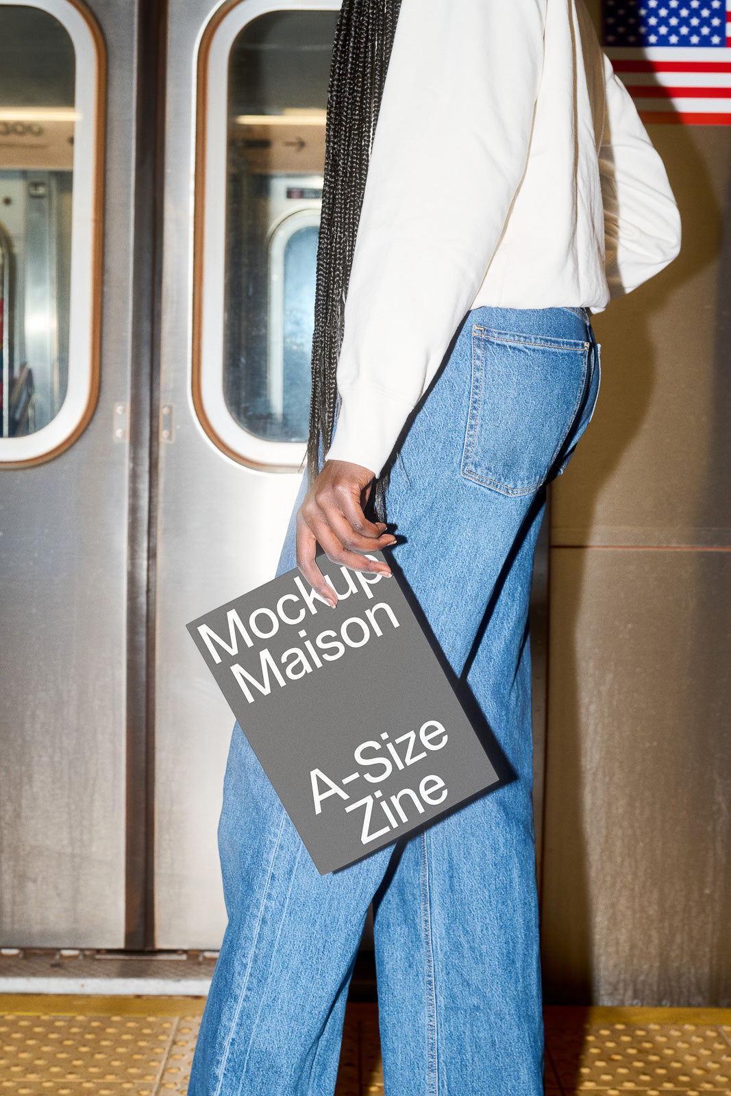 PSD mockup of a person holding a gray zine with "Mockup Maison A-Size Zine" text, standing near a subway door.