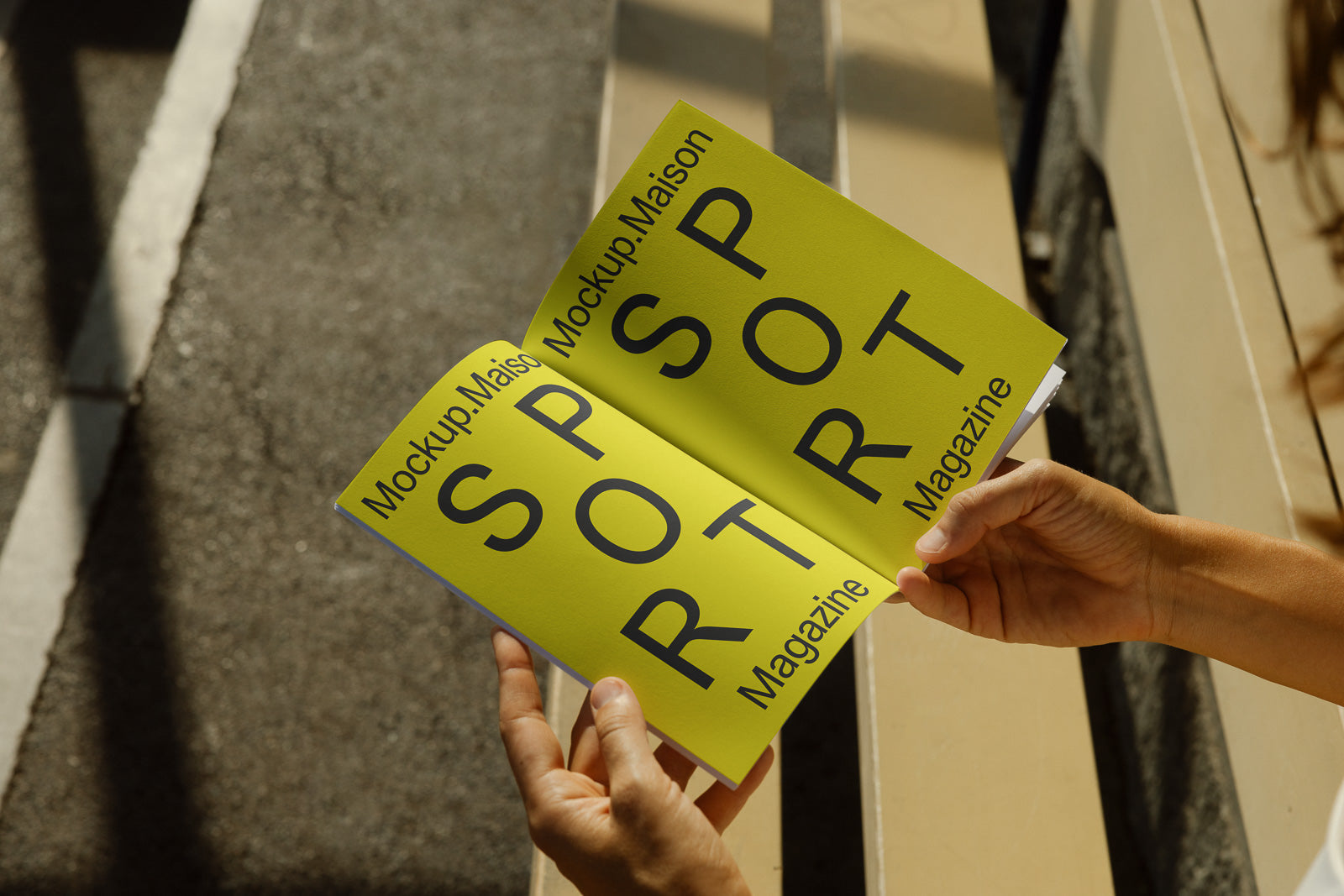 PSD mockup of a person holding a yellow magazine with bold text "SPORT" and "Maison Mockup" visible on the pages.