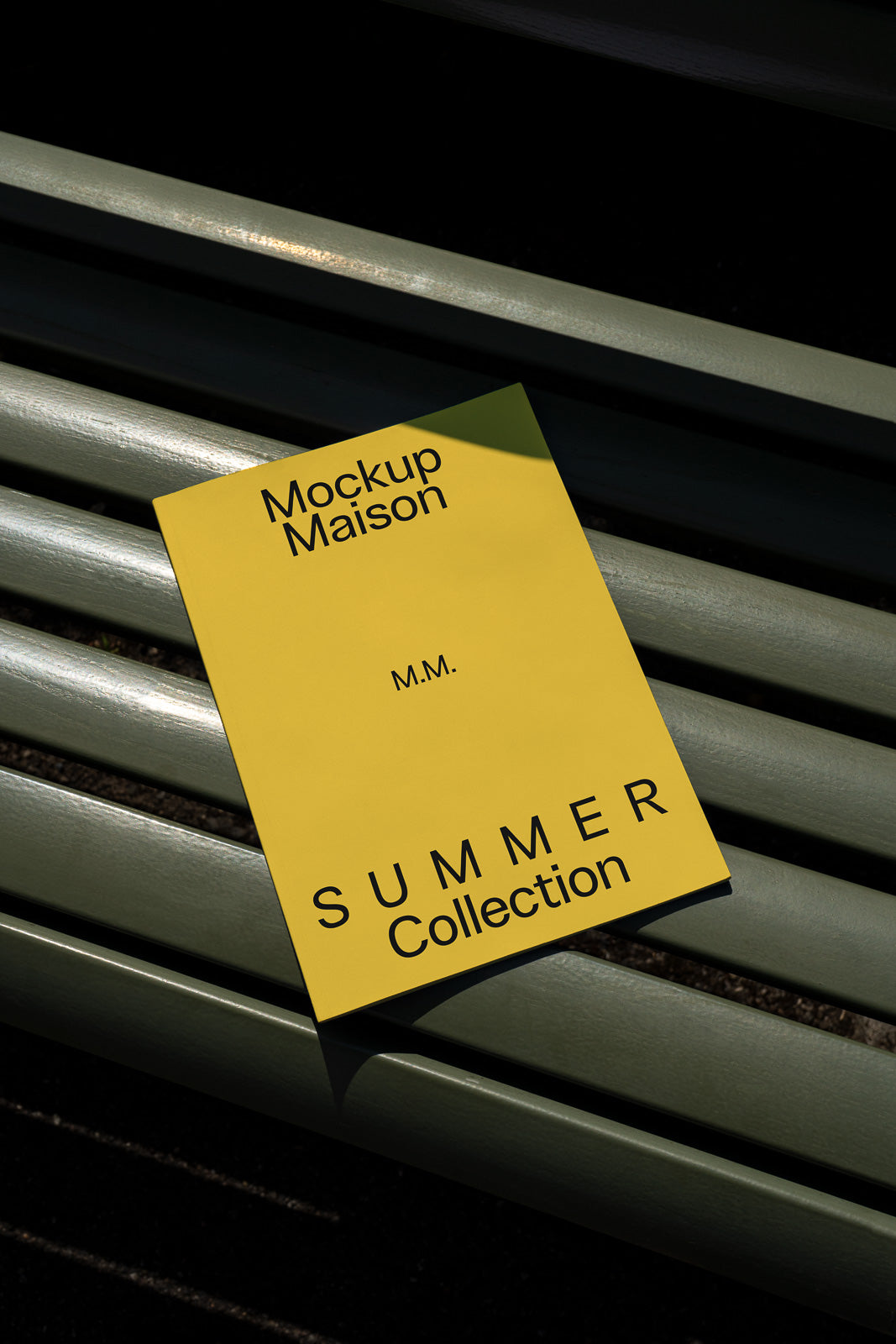 PSD mockup of a yellow booklet titled "Mockup Maison Summer Collection" placed diagonally on a bench, casting a shadow.