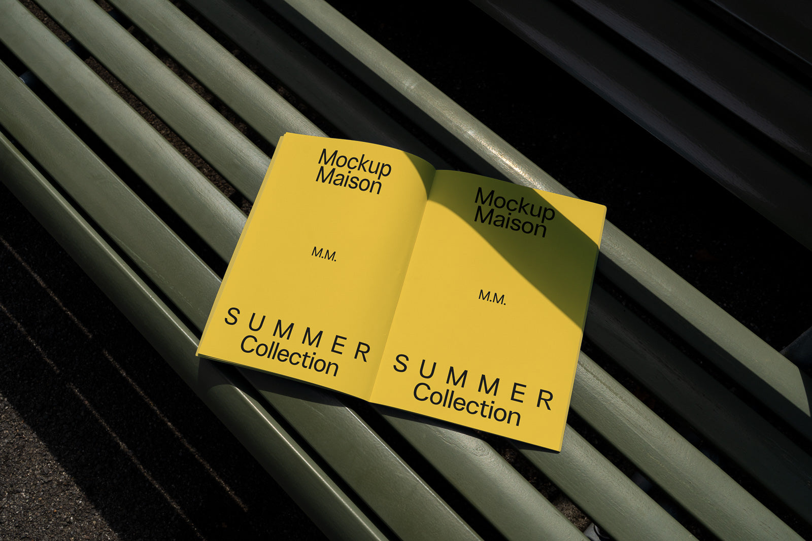PSD mockup of an open yellow magazine titled "Mockup Maison" with "SUMMER Collection" laying on a green bench under sunlight, casting shadows.