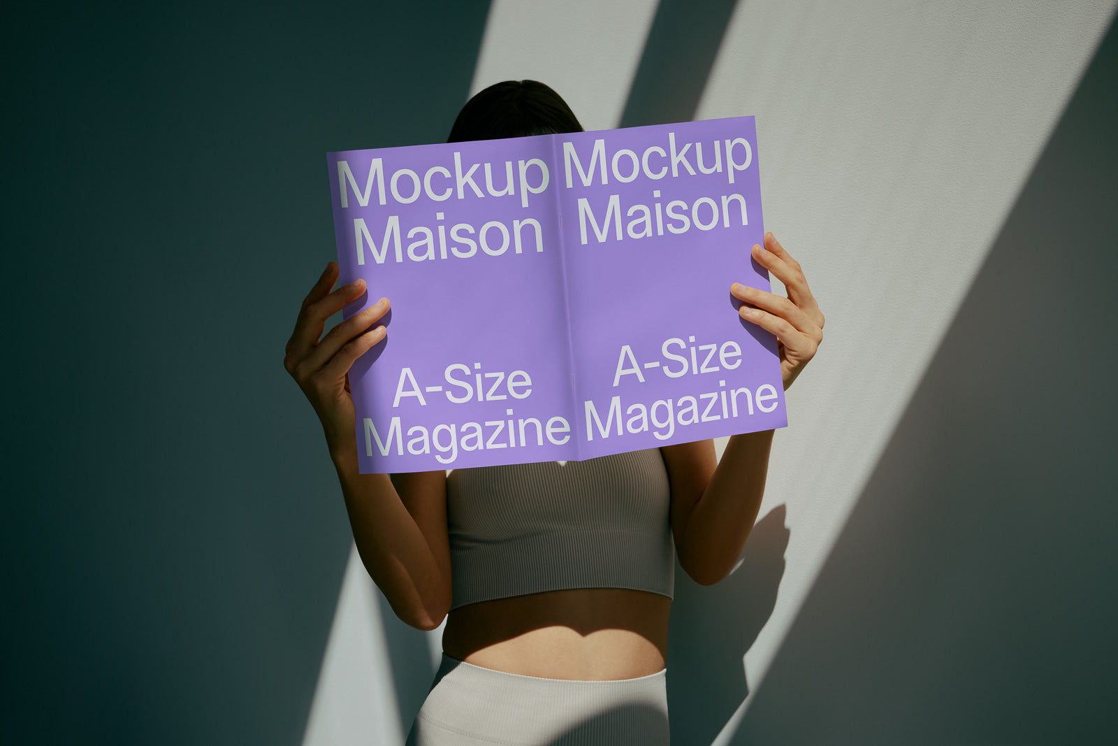 PSD mockup of a person holding an open A-size magazine with a lavender cover, titled "Mockup Maison," against a neutral background.