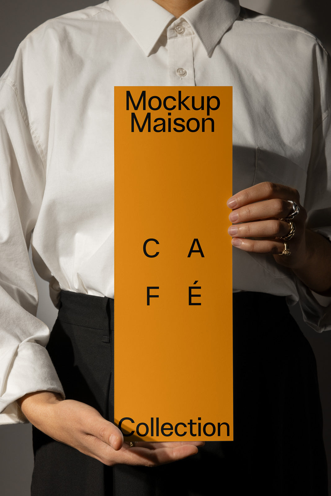 PSD mockup of a person holding an orange rectangular card with black text reading "Mockup Maison," "Café," and "Collection."