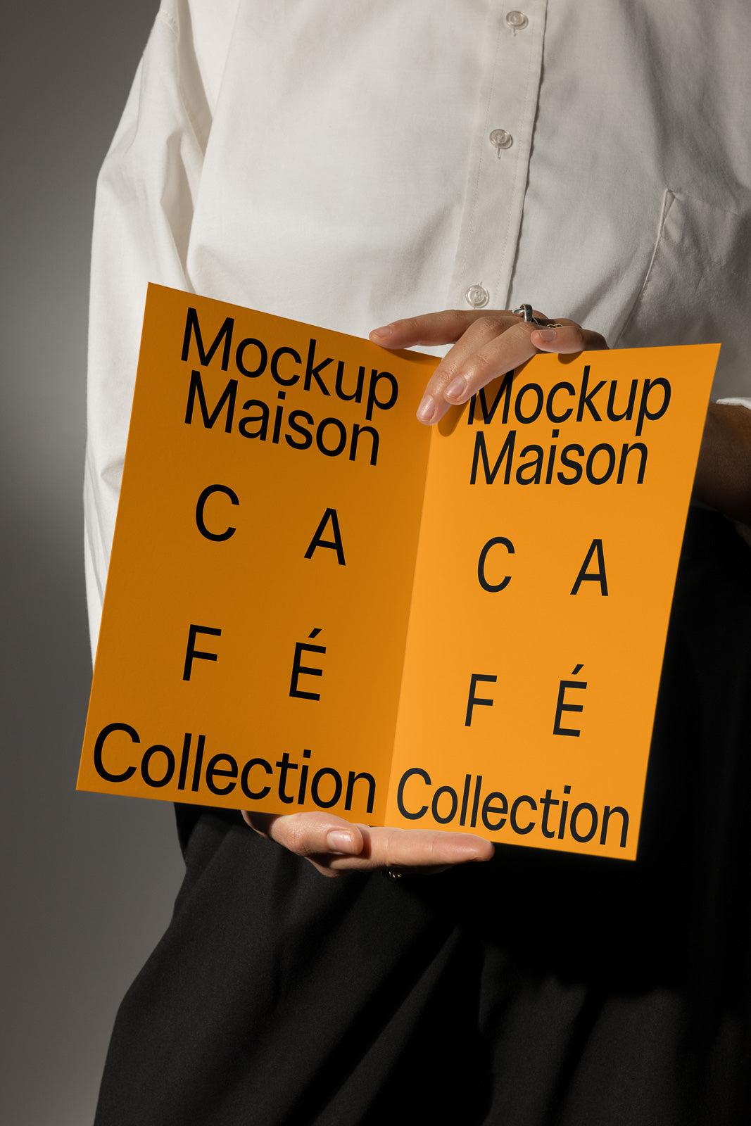 PSD mockup of a person holding an orange brochure with the text "Mockup Maison Café Collection" displayed in bold black font, against a neutral background.