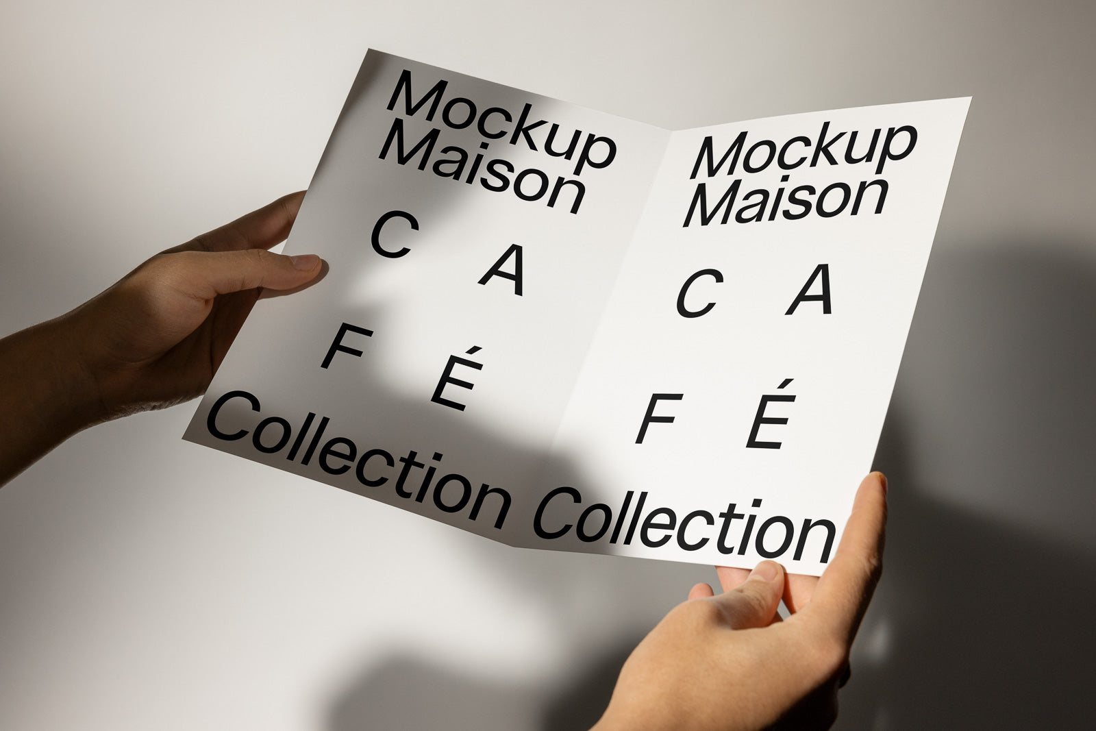 PSD mockup of hands holding an open brochure displaying bold text "Mockup Maison" and "Café Collection" under soft lighting.