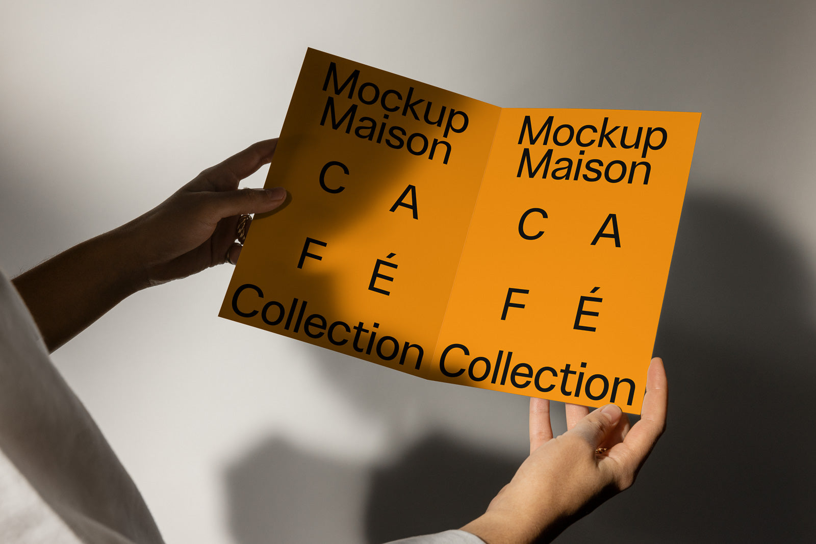 PSD mockup of a person holding an orange booklet with "Mockup Maison Café Collection" text in bold black letters on both pages.