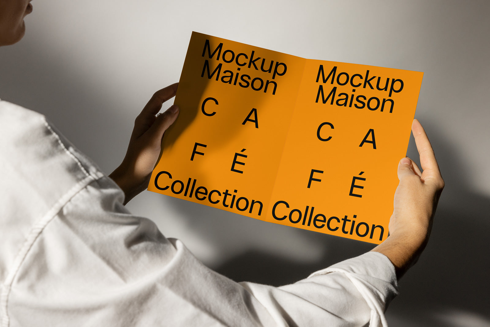 PSD mockup of a person holding an open booklet with the text “Mockup Maison Café Collection” in bold black font on an orange background.