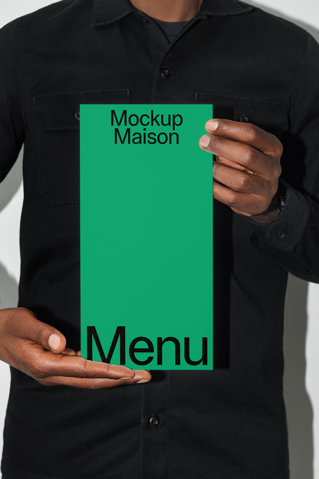 PSD mockup of a person holding a green menu card with "Mockup Maison" text, wearing a black shirt, highlighting minimalist design.