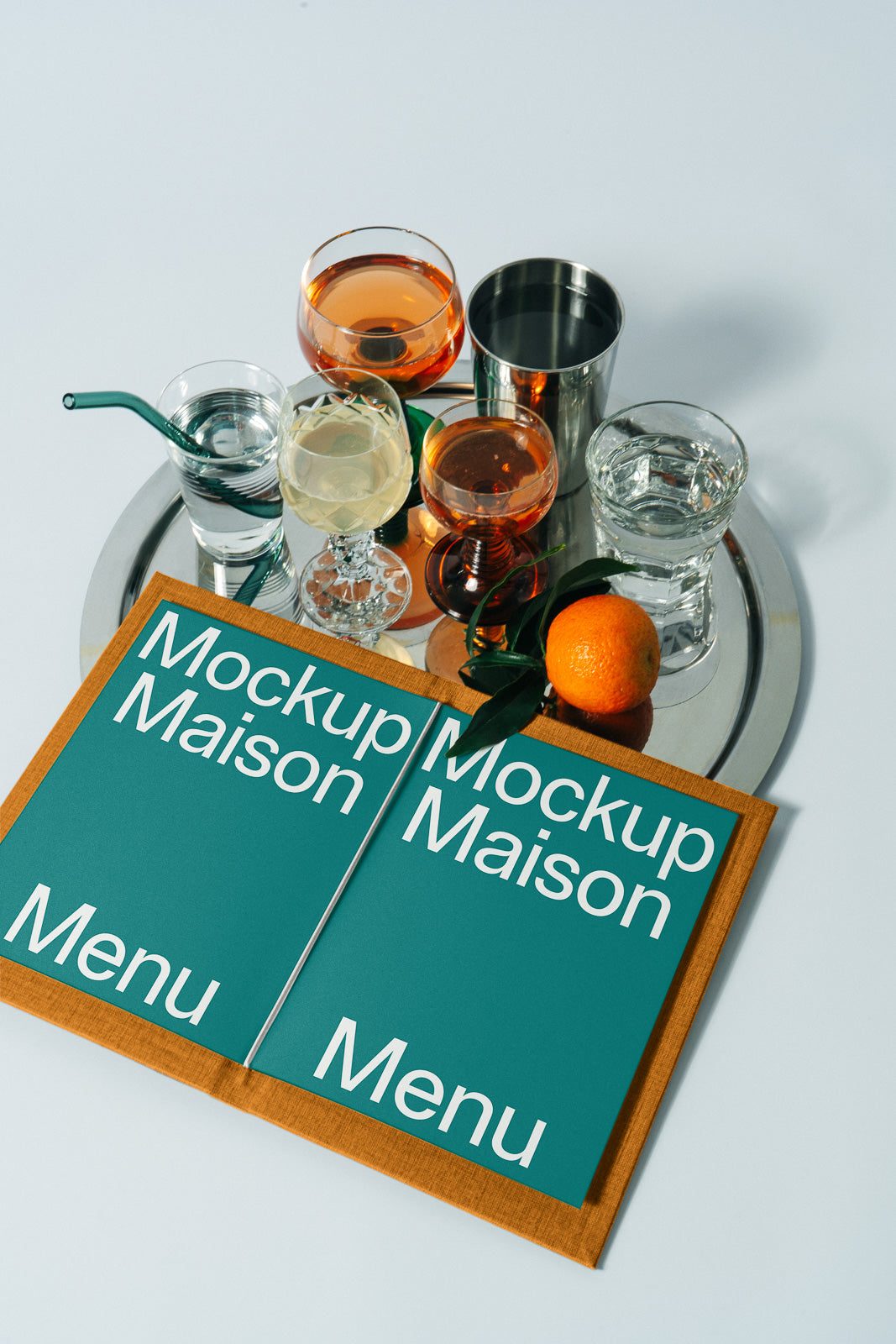 PSD mockup of a menu booklet on a table with a silver tray holding various glasses and an orange, creating an elegant dining scene.